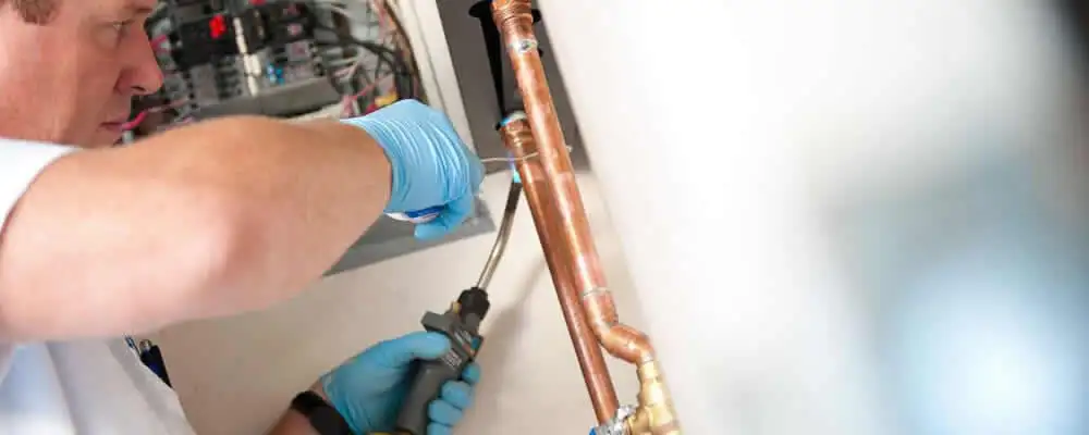 Water heater repair technician testing copper pipe connections and controls in Stockton, CA